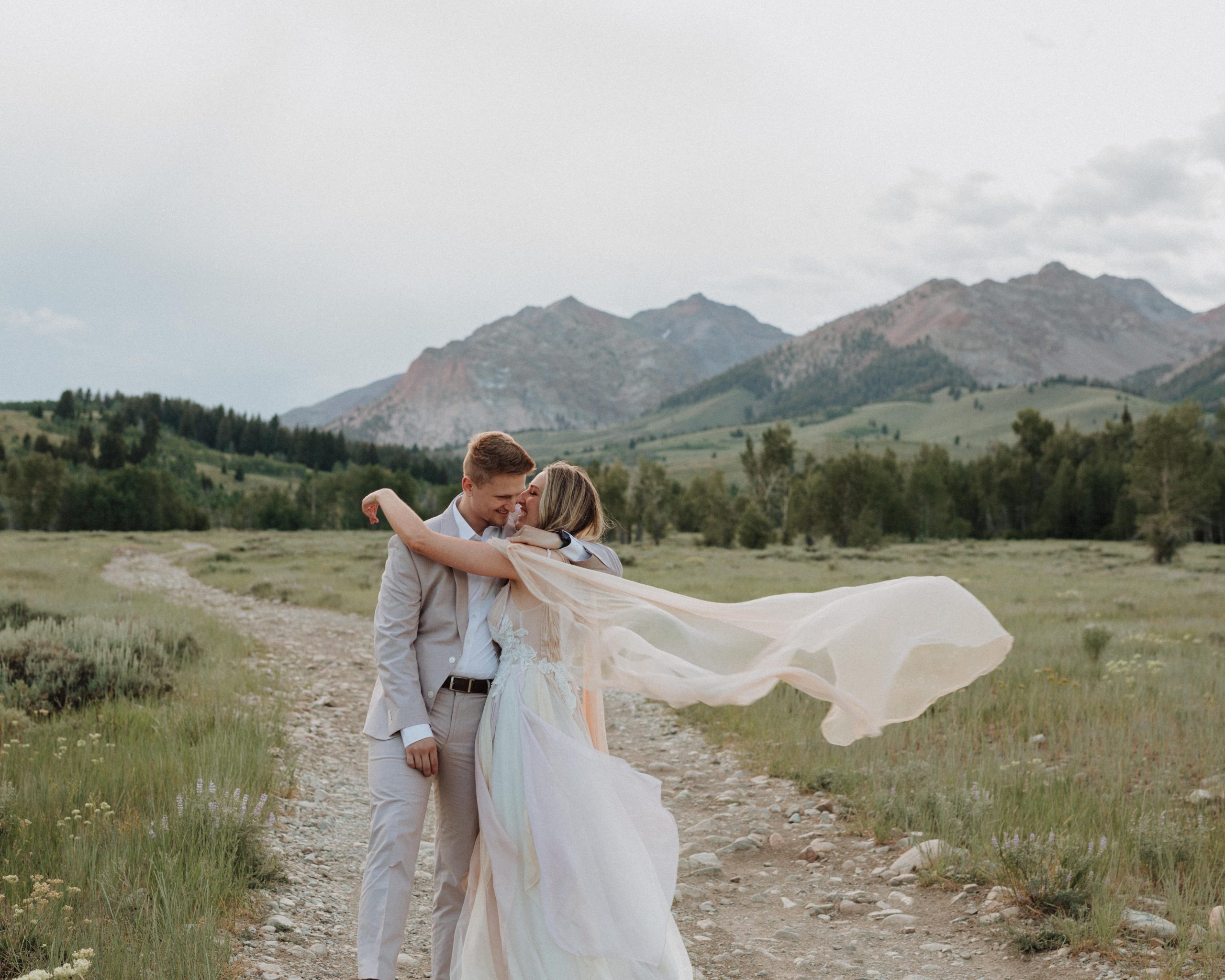 Couple sharing an embrace as the bride's veil flies with the wind at Fishhook Creek Trail
