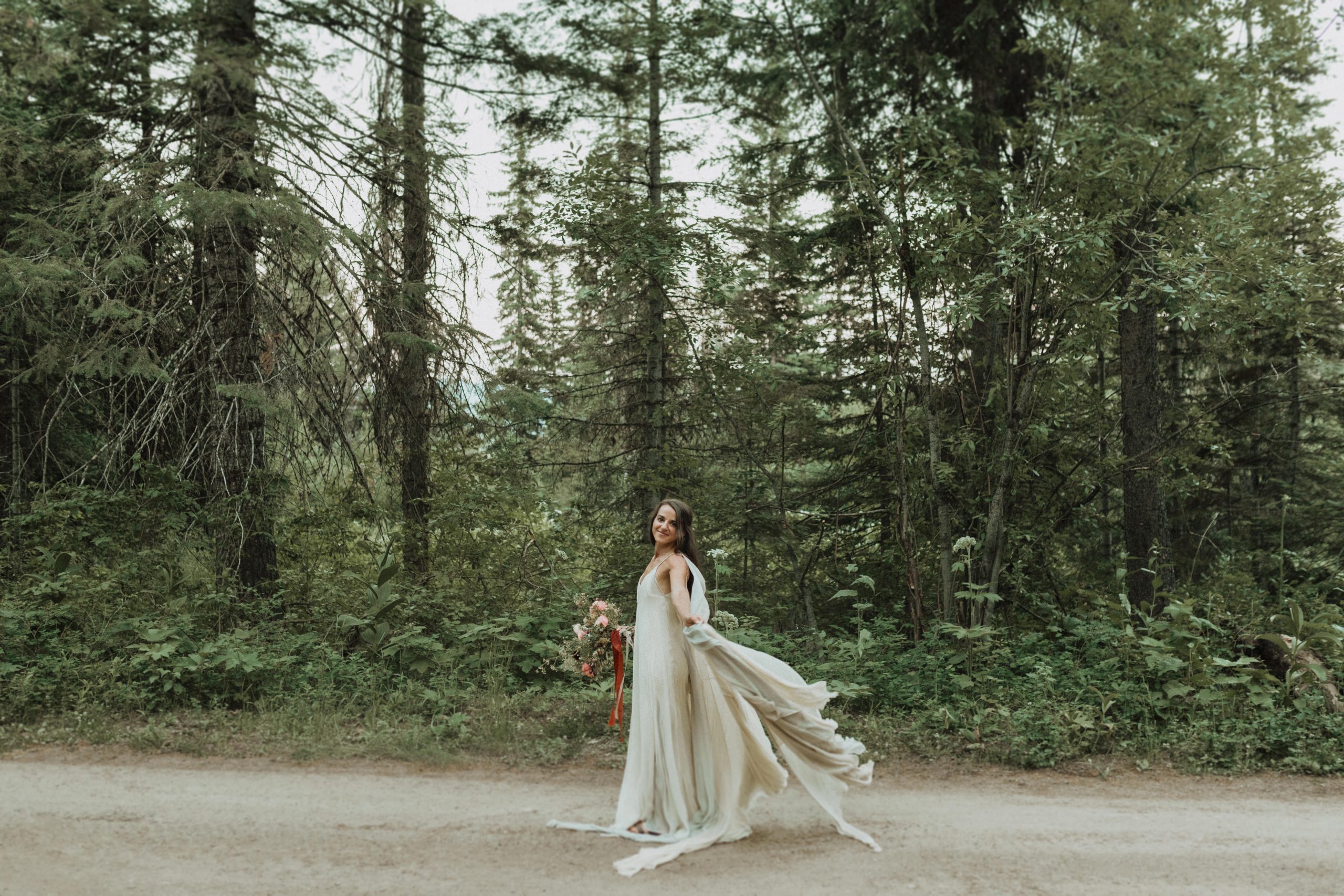 Bride smiles as she sways with her dress while holding her bouquet during her elopement shoot at Boise National Forest