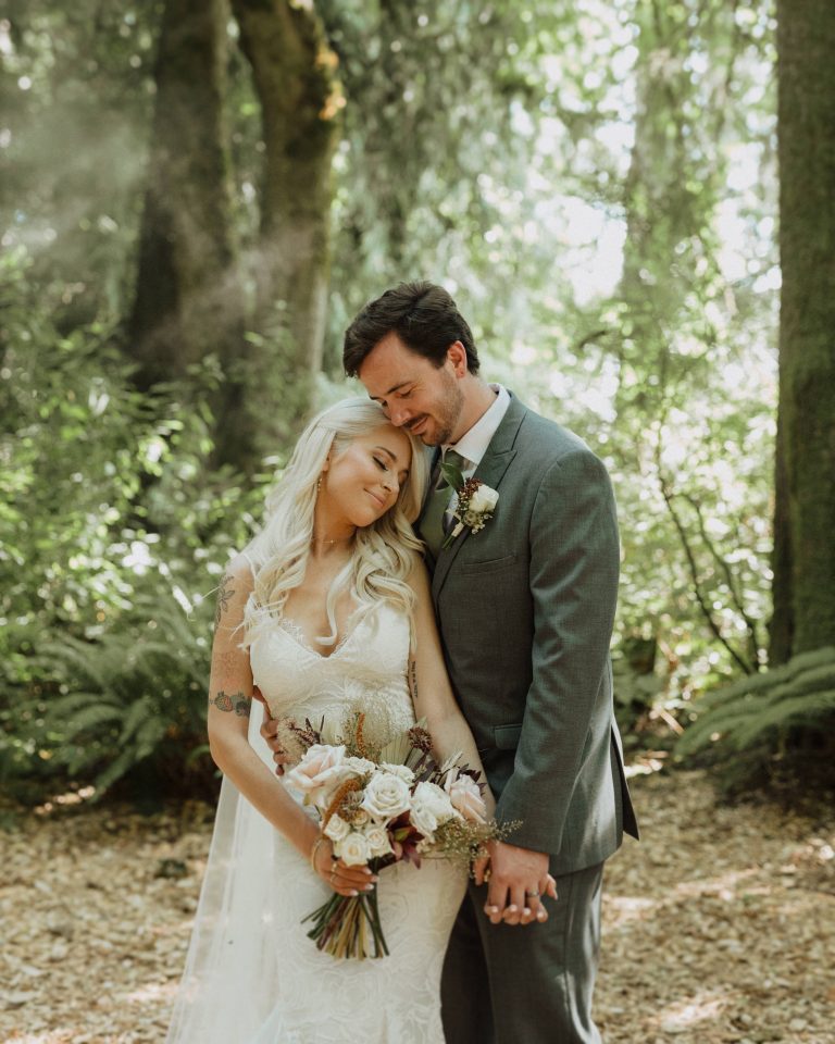 Newlywed couple lean against each other while holding hands at Twin Willow Gardens in Snohomish, WA