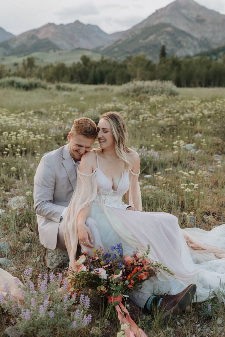Couple share light laughs as they sit together in the field during their elopement shoot in Idaho with Alexa Ann Photography